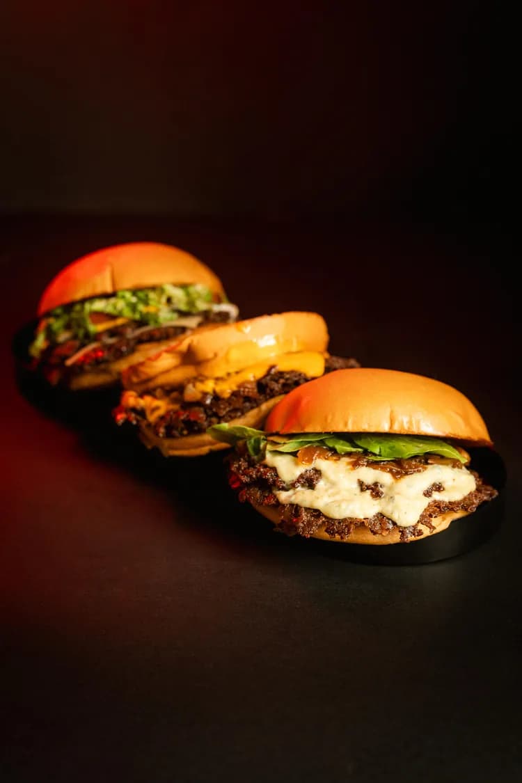 Tres hamburguesas alineadas en fila sobre una bandeja oscura