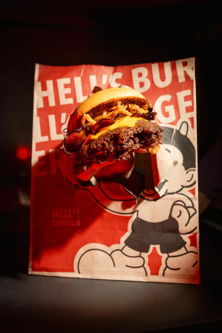 Una hamburguesa doble con cheddar apoyada sobre una bolsa roja de Hell’s Burger