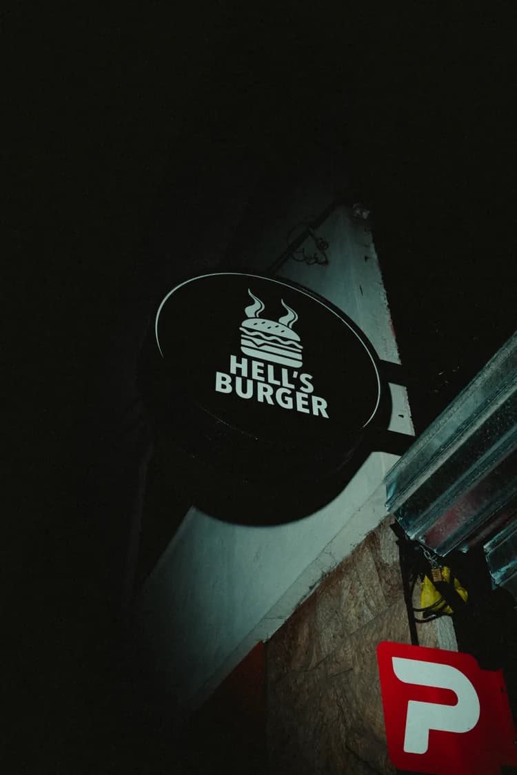 El cartel colgante de Hell’s Burger, con el isotipo de la hamburguesa, en la fachada de noche